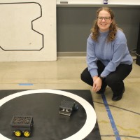 A student kneeling next to a sumo bots project.
